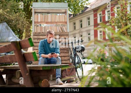 Mature man using smart phone sitting near cabinet of books in suburb Stock Photo