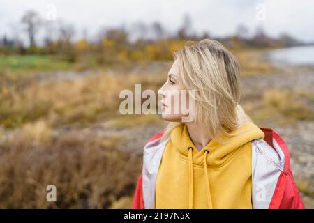 Thoughtful blond woman wearing hooded shirt in autumn park Stock Photo