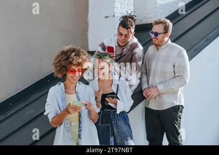 Smiling woman talking and using smart phone with friends on rooftop Stock Photo