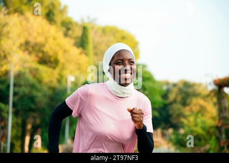 Happy young woman wearing hijab jogging at park Stock Photo