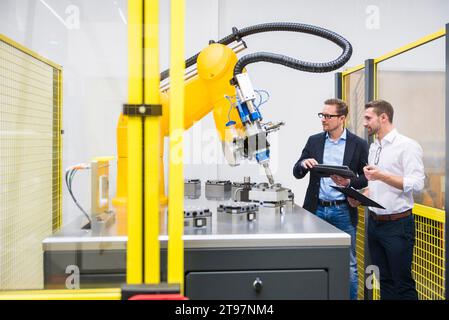 Engineers with tablet PC examining robotic arm in factory Stock Photo