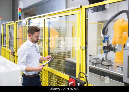 Engineer examining checklist near robotic arm at factory Stock Photo