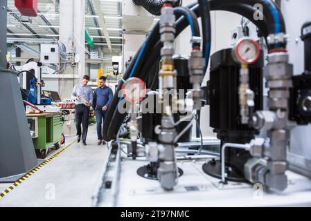 Engineer with machine part explaining to colleague in factory Stock Photo