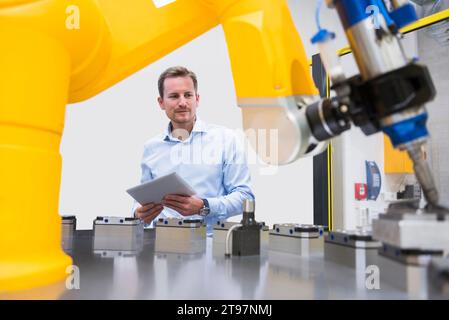 Engineer holding tablet PC and examining robotic arm in factory Stock Photo