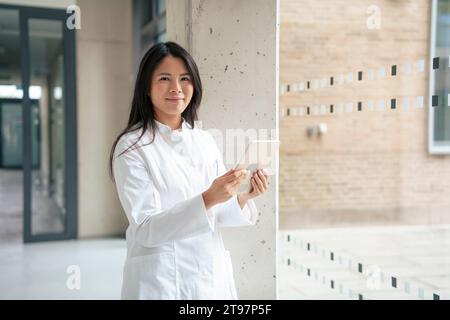 Smiling scientist standing with tablet PC in corridor Stock Photo