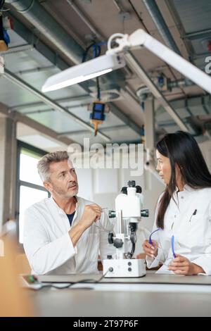 Scientists discussing with microscope at desk in laboratory Stock Photo