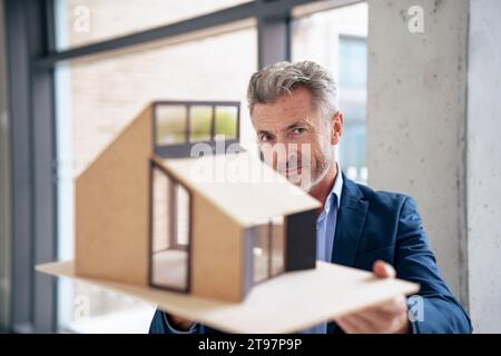 Mature businessman standing with model house in office Stock Photo