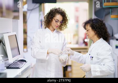 Pharmacist assisting colleague in making medicine using mortar and pestle at laboratory Stock Photo