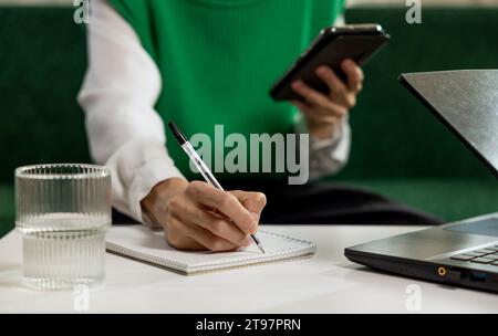 Freelancer taking notes from smart phone at home office Stock Photo
