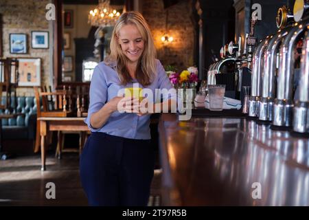 Smiling owner using smart phone near bar counter at pub Stock Photo