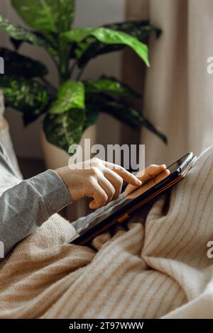 a caucasian man relaxing, using digital tablet lying in bed under throw at home Stock Photo