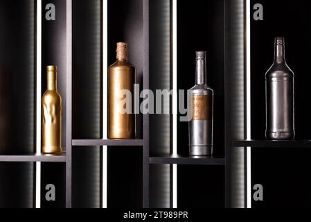 A variety of bottles of alcohol, painted with gold and silver paint, stand on illuminated bar shelves. Decor of a restaurant, bar, banquet hall, bar Stock Photo
