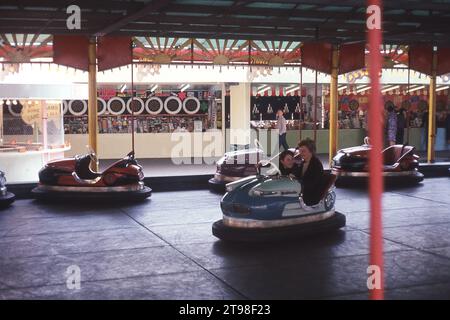 1968, historical, summer and a mother and son having fun together in a dodgem car at a fairground, England, UK. Also known as bumper cars, as these electric powered small cars with rubber bumpers all round are designed to 'bump' into the other such cars and are a  traditonal amusement ride at a British funfair. Stock Photo