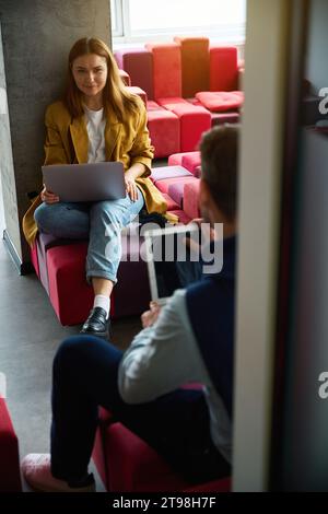 Female and male sit with their laptops on multi-colored sofa Stock Photo