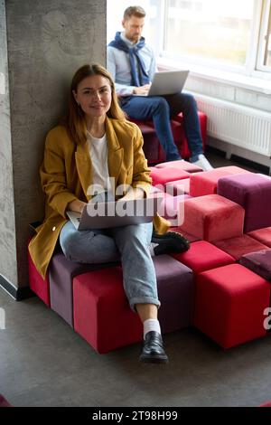 Colleagues sit with laptops on colorful sofas Stock Photo