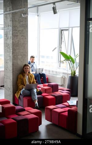 Colleagues managers sit with laptops on multi-colored sofas Stock Photo