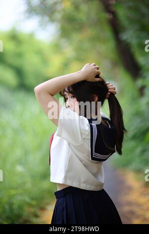 Japanese high school student tied her hair up in park with tree background Stock Photo
