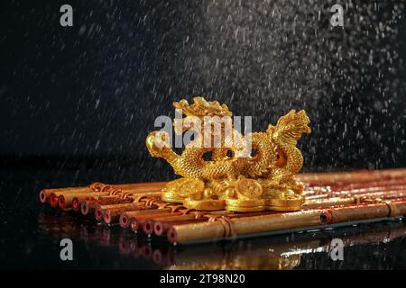 Golden Chinese dragon figurine on bamboo mat under falling water droplets against black background. New Year celebration Stock Photo