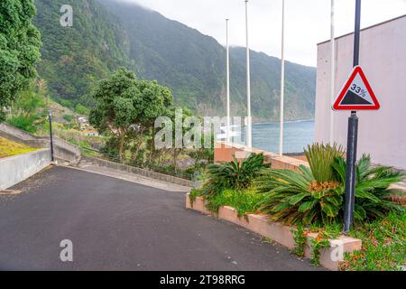 Paved access road to the natural pools of Seixal on Madeira Island. Vertical traffic hazard sign.  road slope with 33% unevenness. Stock Photo