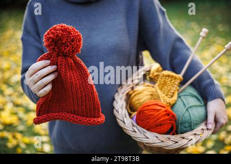 Knitting and crochet. Woman holding handmade red knit hat and balls of wool in basket Stock Photo