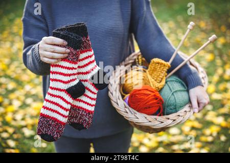 Knitting and crochet hobby. Woman holding handmade pair of knitted socks and colorful balls of wool in basket Stock Photo