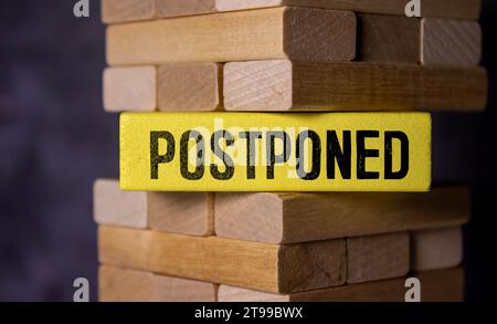 The word POSTPONED is written in a white notepad near a white cup of coffee on a light background. Stock Photo