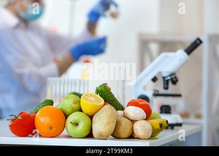 Fresh vegetables, fruits on table and scientist proceeding quality control in laboratory Stock Photo