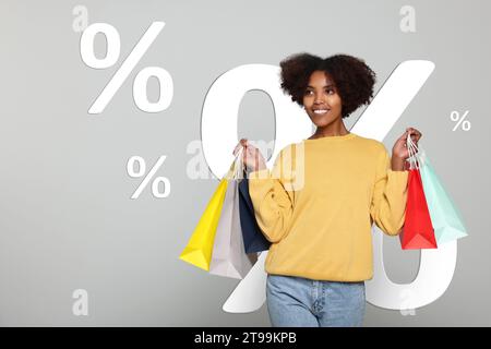 Discount offer. Happy woman with paper shopping bags on light grey background. Illustrations of percent signs behind her Stock Photo