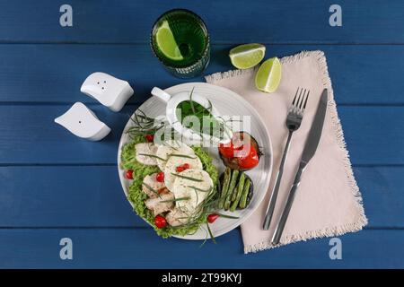 Tasty mozzarella, chicken, vegetables and drink with tarragon served on blue wooden table, flat lay Stock Photo