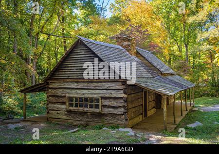 Seen from a few steps back, the cabin's gable window and porch posts sit among yellow and orange leaves in Great Smoky Mountains National Park. Stock Photo
