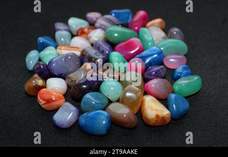 Colored rough gemstones in a heap of black surface detailed angle view with soft focus Stock Photo