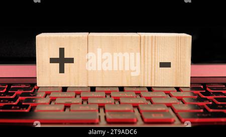 business concept.. Plus, minus symbols the inscription on wooden cubes on the laptop keyboard. Stock Photo