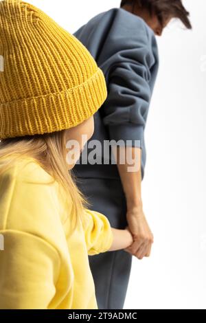 Young mother and little daughter walking holding hands. Dressed in yellow and ment color suits on white background, studio. Concept of advertising positive and clothes. High quality photo Stock Photo