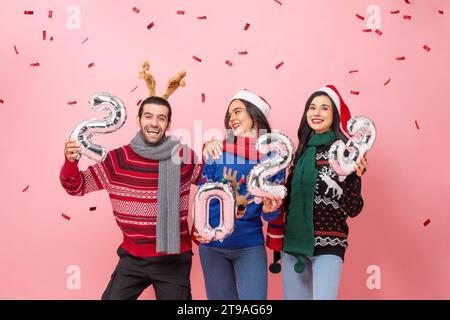 Group of happy male and female friends wearing sweaters celebrating Christmas 2023, studio shot portrait in pink color background Stock Photo