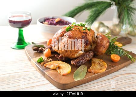 Roast chicken from the oven with fruits and herbs, served with red cabbage and wine on a wooden board, pine branches and Christmas decoration, holiday Stock Photo