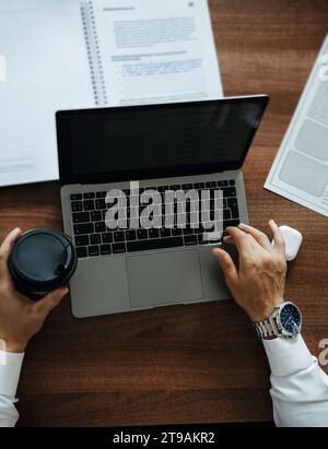Businessman with a cup of coffee in his hands working at a laptop sitting at the table Stock Photo