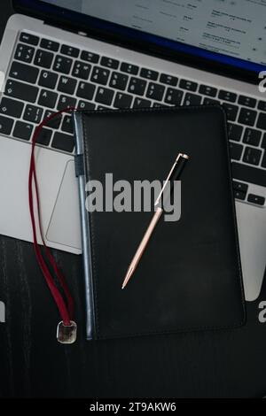 a silver pen and a black notepad lie on the laptop keyboard Stock Photo
