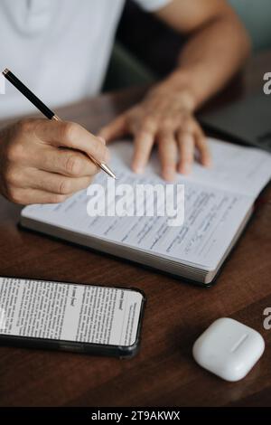 Man makes entries in a diary, close-up hands notepad and phone on the table Stock Photo
