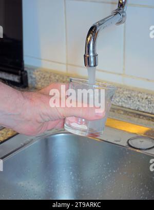 Hand holding a glass of water poured from the kitchen faucet Stock Photo