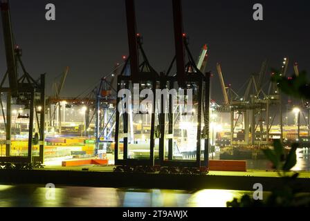 Industrial cranes and containers at a busy harbor at night, illuminated by work lights. Stock Photo