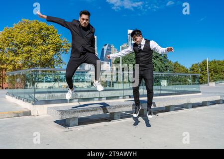 Young Hispanics having fun and jumping from a bench in a public park. Formal wear Stock Photo