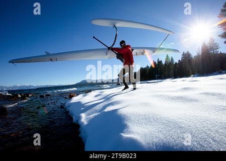 One man walking his outrigger canoe over snow to a mountain lake in winter. Stock Photo