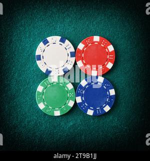 Casino background with detail of four different colored plastic chips centered on green felt gaming mat. Top view. Square composition Stock Photo