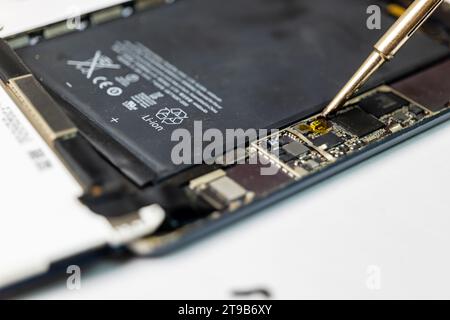 technician carefully repairs a damaged tablet's soldering components using a variety of specialized tools Stock Photo