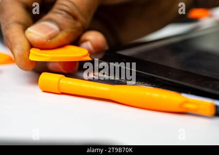 A skilled technician meticulously removes a tablet's display using specialized tools Stock Photo