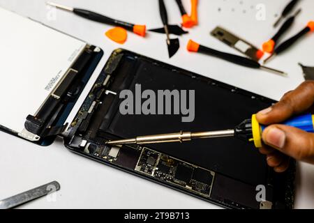 technician meticulously solders a tablet component using specialized tools in a well-lit workspace Stock Photo