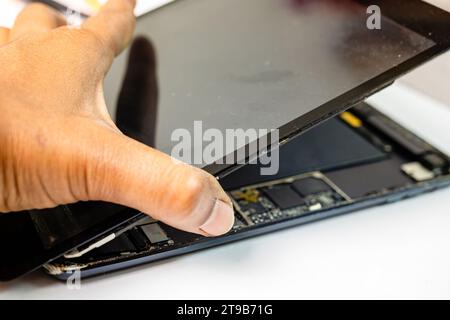 A skilled technician meticulously separates the cracked display from a tablet device using specialized tools Stock Photo