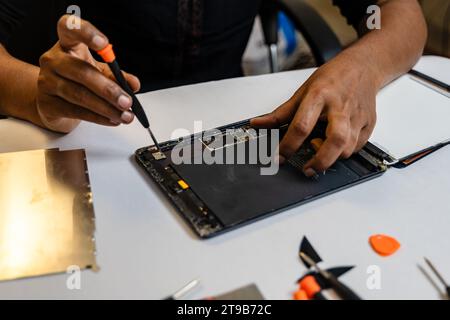 A technician is carefully repairing a tablet with a variety of tool kits. They are using a screwdriver to open the tablet Stock Photo