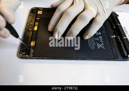 A concentrated technician meticulously disassembles a tablet using a variety of specialized tools Stock Photo