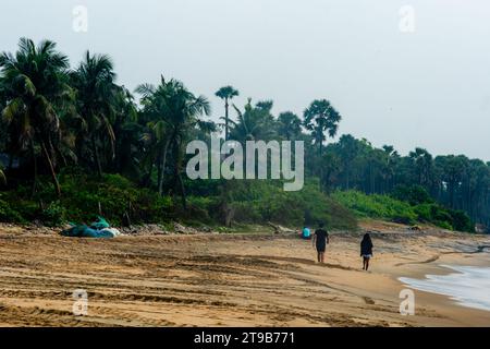 A man and a woman walk along a beach littered with plastic bottles, bags Stock Photo